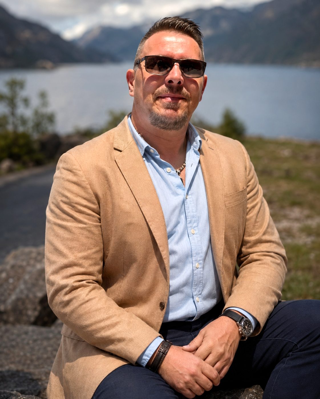 Janne Engman in a sand-coloured blazer, seated outdoors with a fjord landscape behind him.